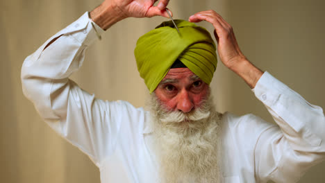 Fotografía-De-Estudio-De-Un-Hombre-Sikh-Mayor-Con-Barba-Que-Usa-Una-Aguja-De-Salai-Mientras-Se-Pone-Un-Turbante-Contra-Un-Fondo-Liso,-Filmada-En-Tiempo-Real-1